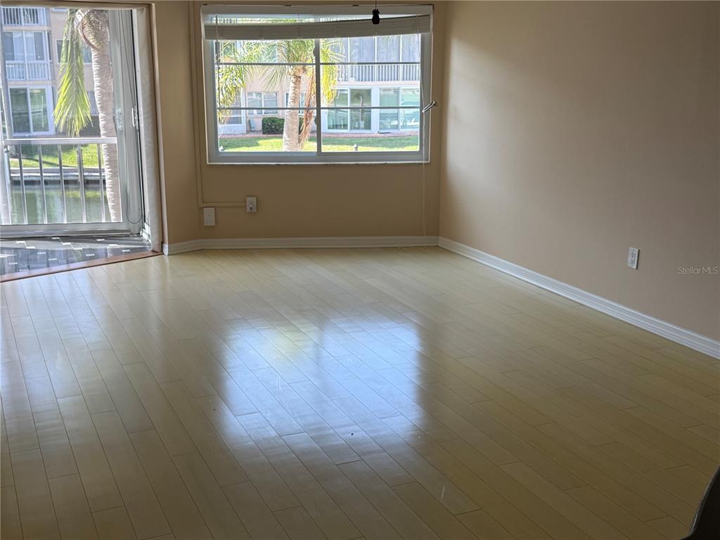 An empty room with light wood flooring, a large window, and a sliding glass door — 1250 N PORTOFINO DRIVE UNIT 202, SARASOTA, FL