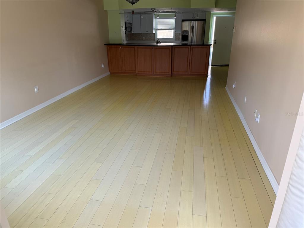 An open-concept living area features light-colored hardwood flooring and a kitchen with wooden cabinets — 1250 N PORTOFINO DRIVE UNIT 202, SARASOTA, FL