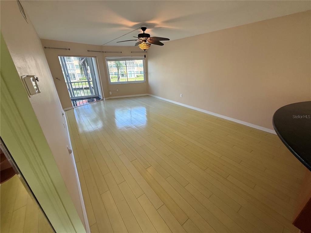 An empty living room features light-colored wood flooring, a ceiling fan, and a sliding glass door — 1250 N PORTOFINO DRIVE UNIT 202, SARASOTA, FL