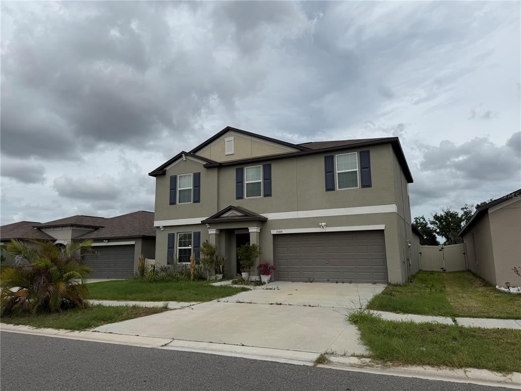 A two-story suburban house with a tan stucco exterior, dark shutters, and a two-car garage — 15434 MILLER CREEK DRIVE, SUN CITY CENTER, FL