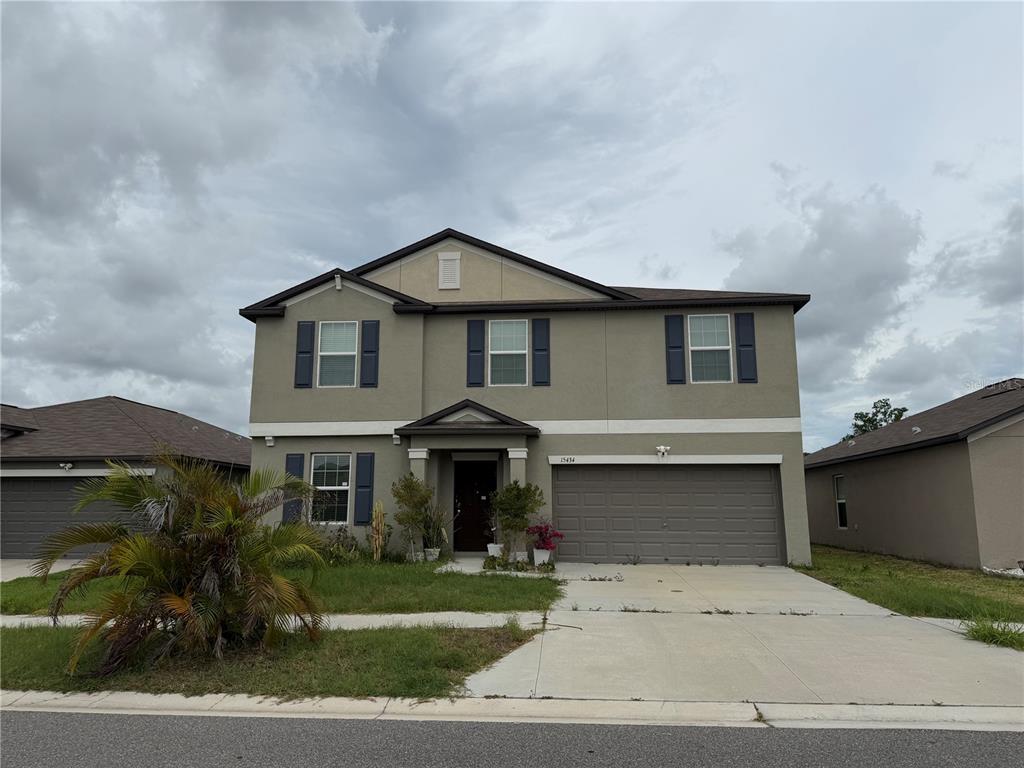 A two-story suburban house with a tan stucco exterior, dark shutters, and a two-car garage — 15434 MILLER CREEK DRIVE, SUN CITY CENTER, FL