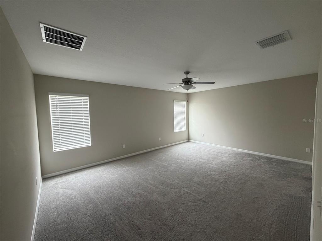 An empty bedroom features beige walls, gray carpeting, two windows with blinds, and a ceiling fan — 15434 MILLER CREEK DRIVE, SUN CITY CENTER, FL