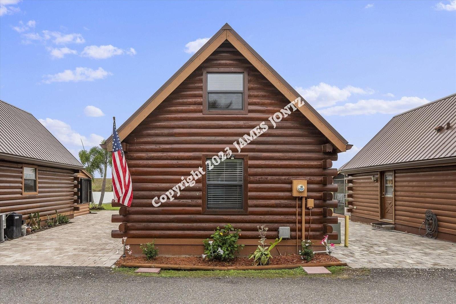 A log cabin exterior features a gabled roof, an American flag, and paved walkways — 8344 US Highway 441, Okeechobee FL 34974, OKEECHOBEE, FL