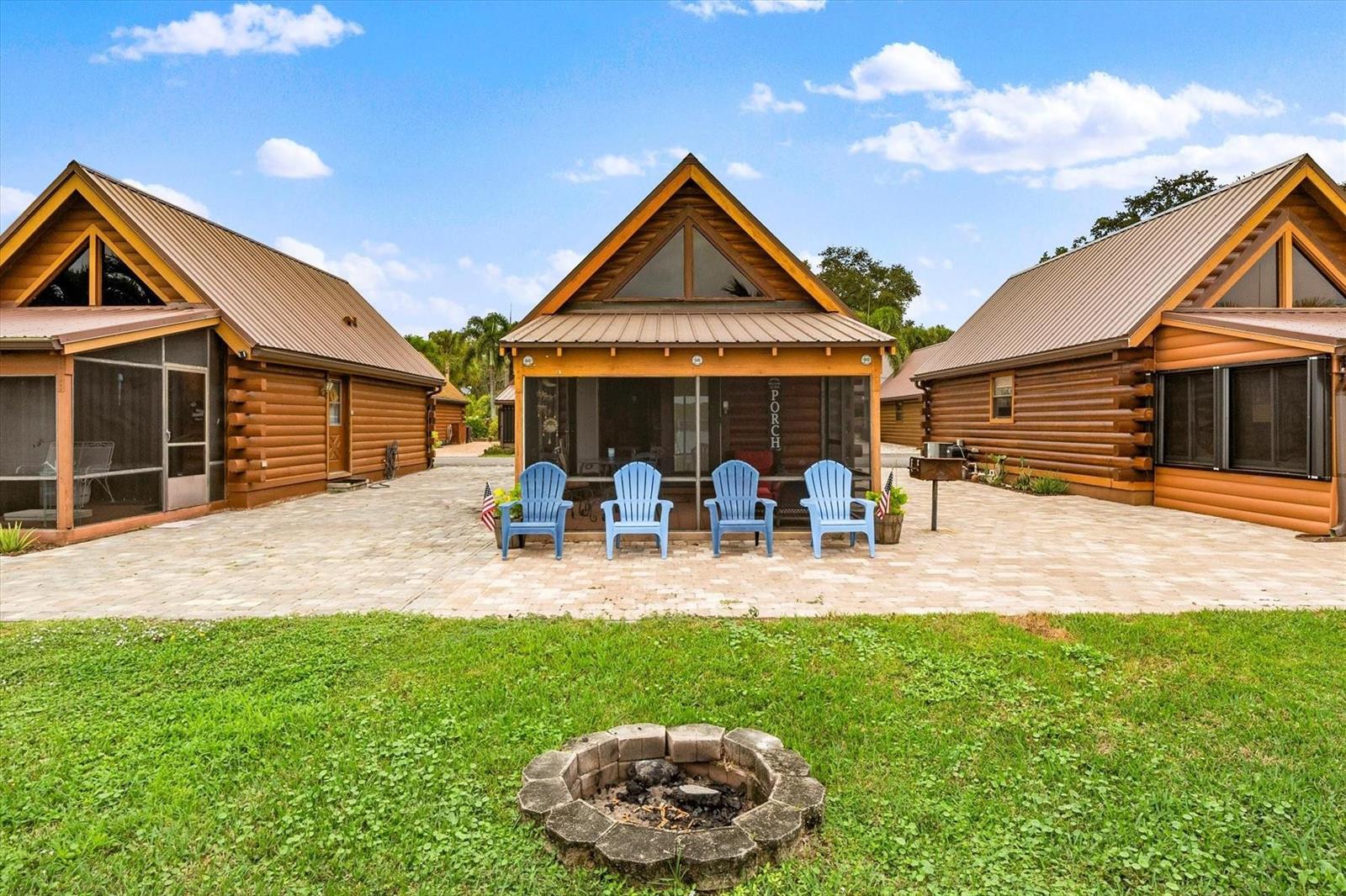 Three log cabins with metal roofs sit behind a stone fire pit and patio — 8344 US Highway 441, Okeechobee FL 34974, OKEECHOBEE, FL