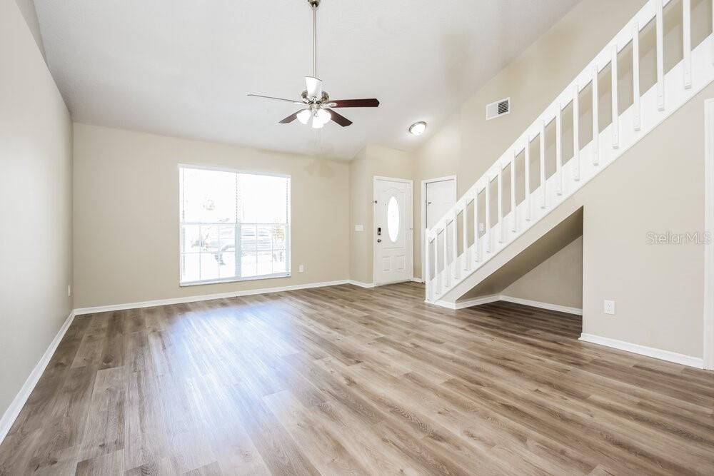 An empty living room features light wood-look flooring, a ceiling fan, and a staircase — 1839 BLAINE TERRACE, WINTER PARK, FL