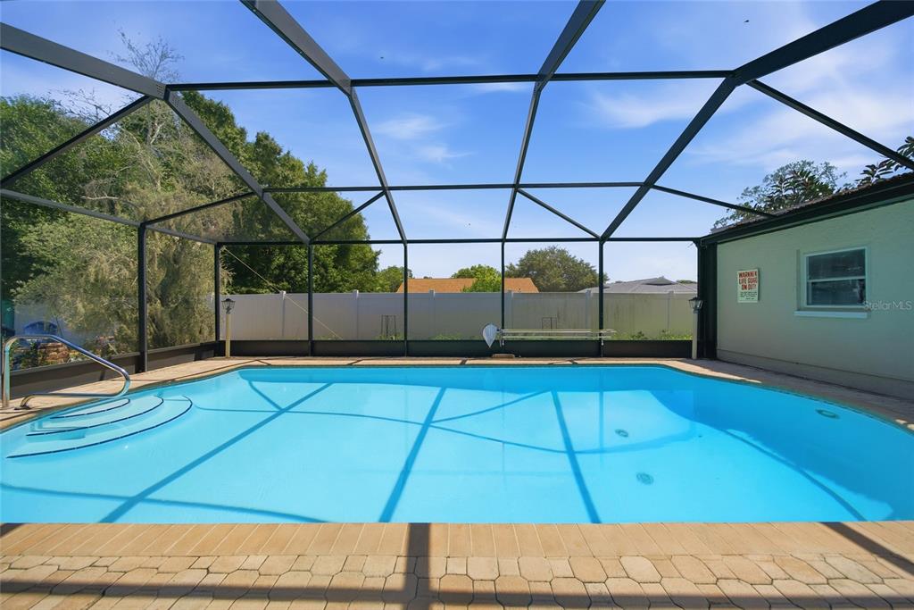 A screened-in swimming pool with steps sits in a backyard enclosed by a white fence — 1403 GARDEN AVENUE, TARPON SPRINGS, FL
