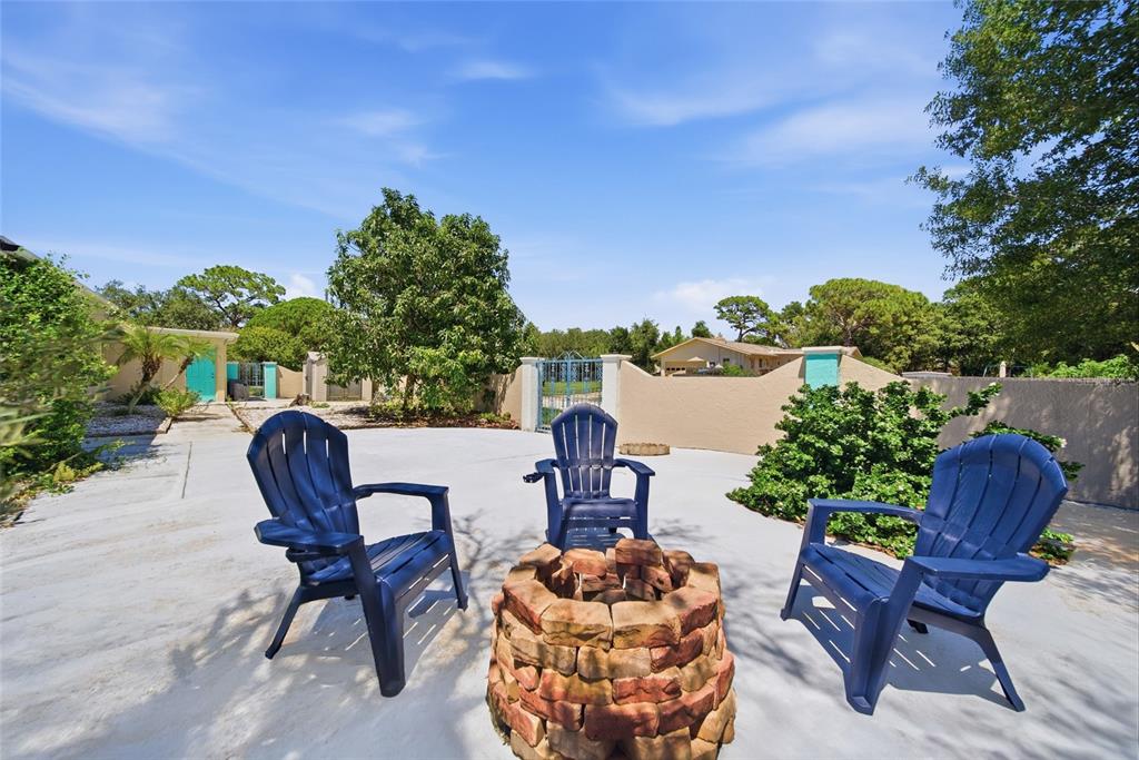 A backyard patio features three blue Adirondack chairs arranged around a circular stone fire pit — 1403 GARDEN AVENUE, TARPON SPRINGS, FL