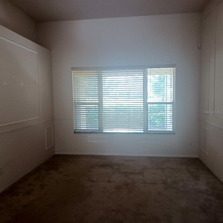 An empty room features beige carpeting, white walls with wainscoting, and a large window — 3807 BEACON RIDGE WAY, CLERMONT, FL