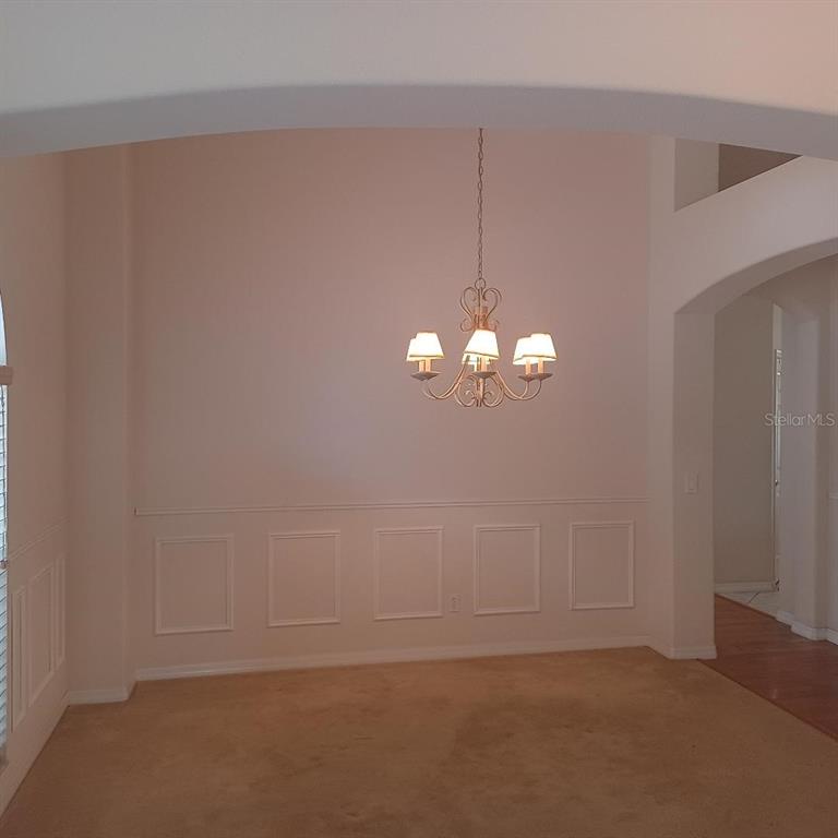 A dining room features beige carpet, white wainscoting, and a hanging chandelier — 3807 BEACON RIDGE WAY, CLERMONT, FL