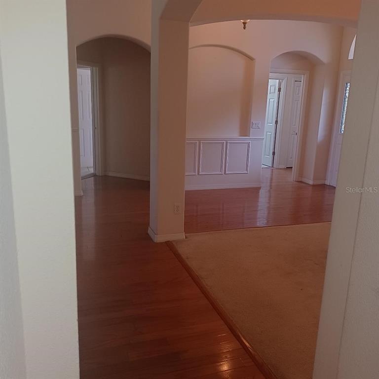 An interior view shows a hallway with hardwood floors leading to rooms with carpeted areas — 3807 BEACON RIDGE WAY, CLERMONT, FL