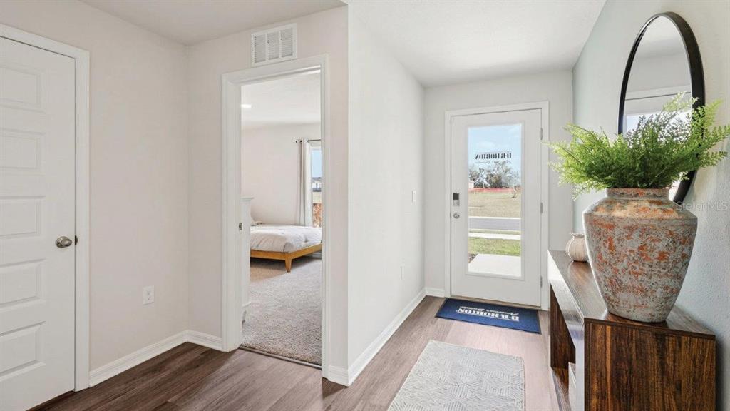 An entryway features wood-look flooring, a white front door, and a view into a bedroom — 746 GREENWAY BOULEVARD, LAKE WALES, FL