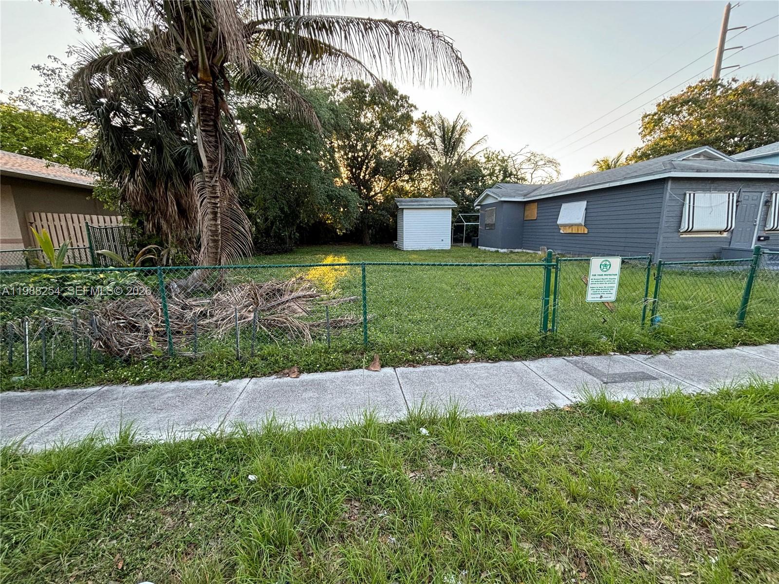 A fenced yard with a small shed and a gray house sits behind a sidewalk — 214 SW 1st Ave, Dania Beach FL 33004, DANIA BEACH, FL