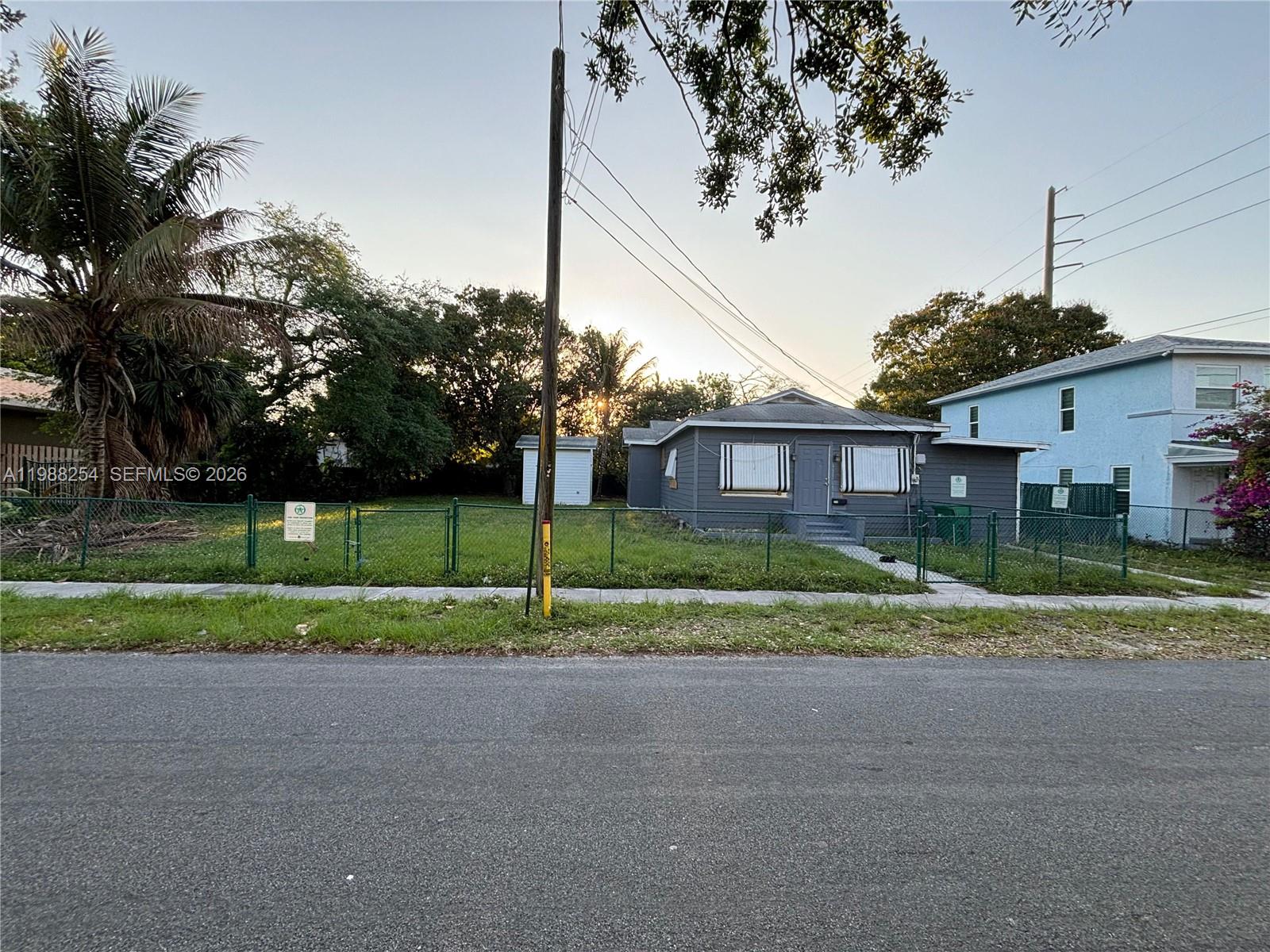 A gray house sits behind a chain-link fence next to a large palm tree — 214 SW 1st Ave, Dania Beach FL 33004, DANIA BEACH, FL