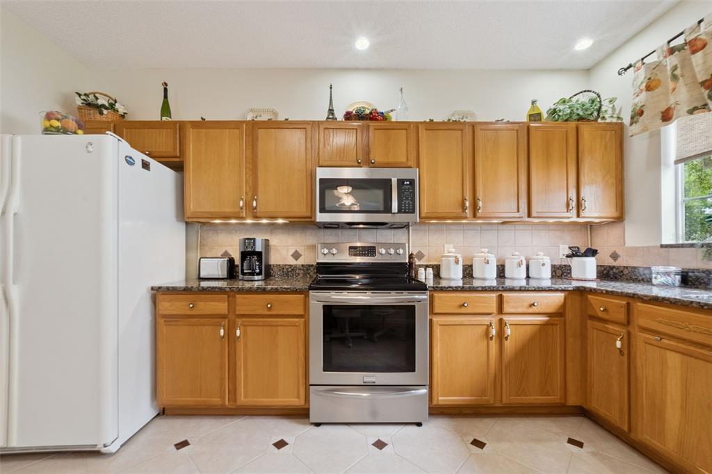 A kitchen features oak cabinets, stainless steel appliances, granite countertops, and light-colored tile flooring — 25239 CRANES ROOST CIRCLE, LEESBURG, FL