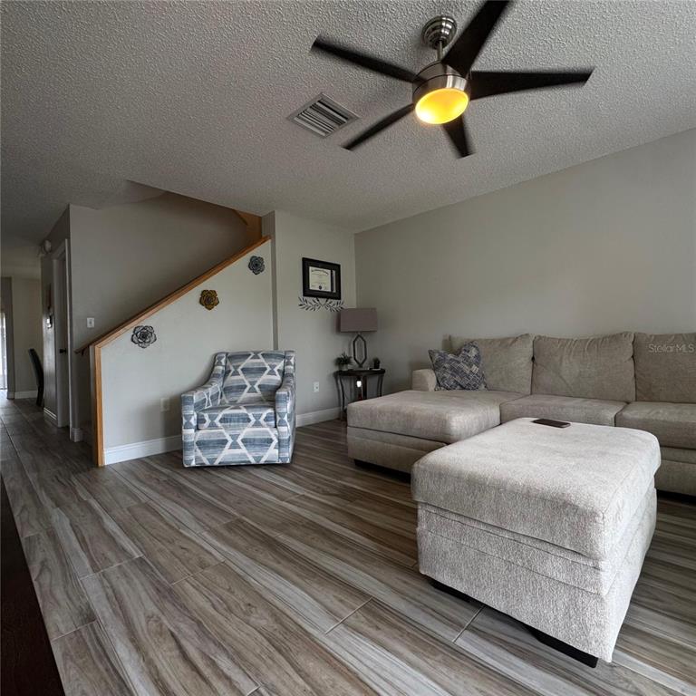 A living room features a sectional sofa, patterned armchair, wood-look tile flooring, and a ceiling fan — 306 KENSINGTON LAKE CIRCLE, BRANDON, FL