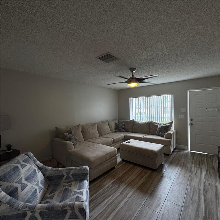 A living room features a beige sectional sofa, an ottoman, and a patterned armchair — 306 KENSINGTON LAKE CIRCLE, BRANDON, FL