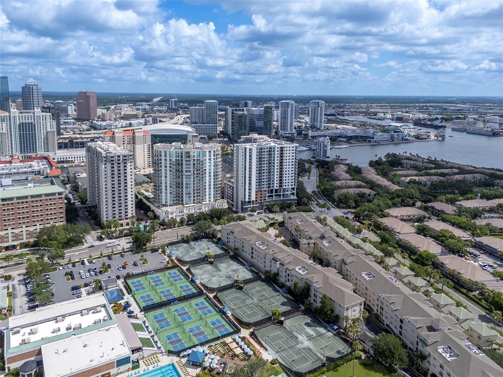 An aerial view shows high-rise apartment buildings, tennis courts, and a waterfront city skyline — 450 KNIGHTS RUN AVENUE UNIT 1503, TAMPA, FL