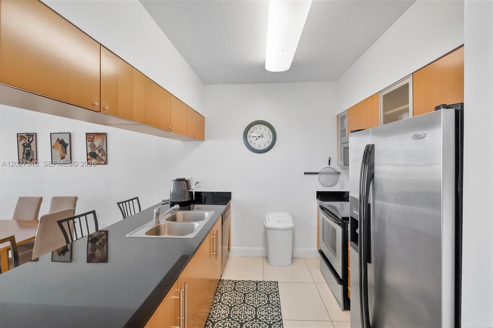 A galley kitchen features light wood cabinets, black countertops, stainless steel appliances, and tile flooring — 1750 N Bayshore Dr # 3106, Miami FL 33132, MIAMI, FL