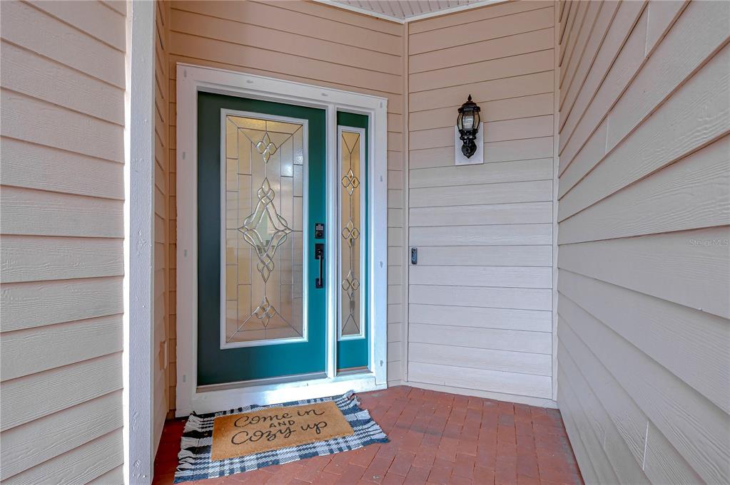 A teal front door with glass panels sits on a brick porch with beige siding — 208 ELM VIEW COURT, BRANDON, FL
