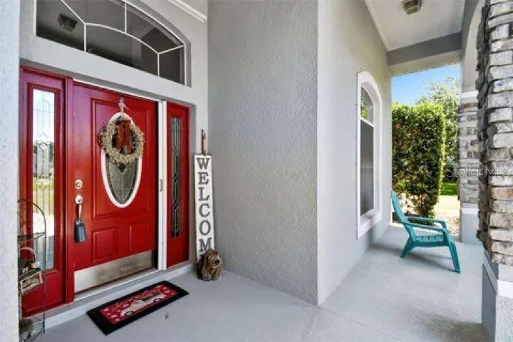 A red front door with a wreath and welcome sign sits on a covered porch — 1900 GRIFF WOOD COURT, ST CLOUD, FL