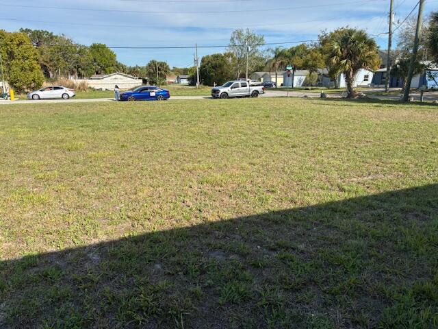 A large, grassy vacant lot is shown with a street and several vehicles in the background — 27344 Elkwood Circle, Hudson FL 34667, HUDSON, FL