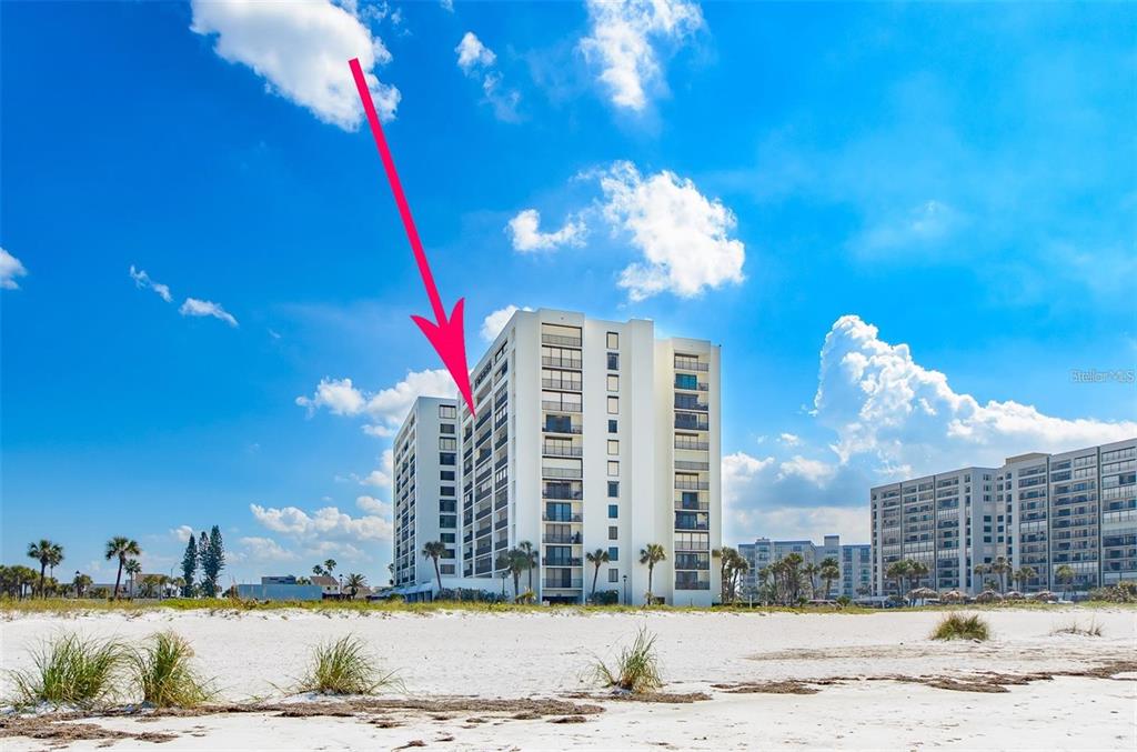 A tall white beachfront condominium building stands behind a sandy beach under a blue sky — 1460 GULF BOULEVARD UNIT 1105, CLEARWATER BEACH, FL