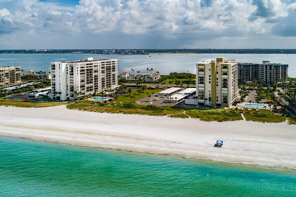 An aerial view of two beachfront apartment buildings with pools and parking lots near water — 1460 GULF BOULEVARD UNIT 1105, CLEARWATER BEACH, FL