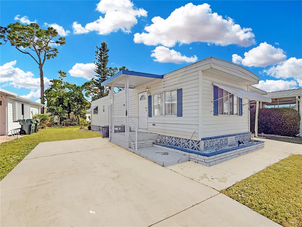 A white mobile home with blue shutters and a concrete driveway under a cloudy sky — 5559 HOLIDAY PARK BOULEVARD, NORTH PORT, FL