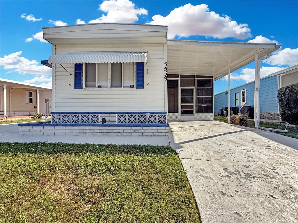 A single-story mobile home features white siding, blue shutters, and an attached carport — 5559 HOLIDAY PARK BOULEVARD, NORTH PORT, FL
