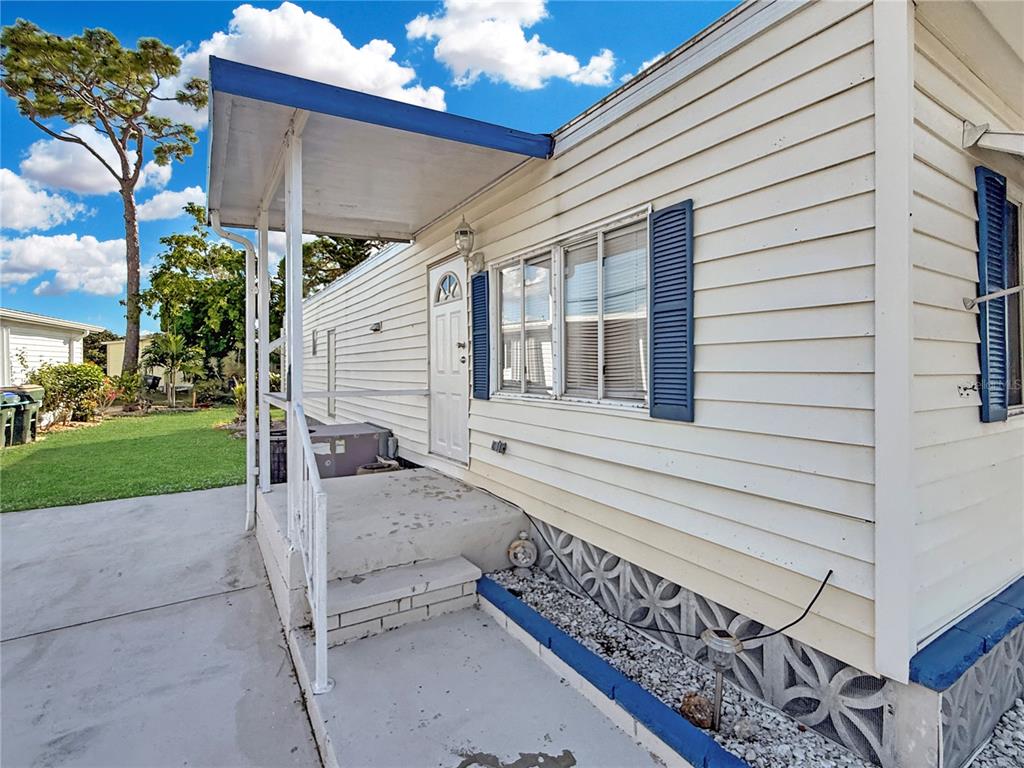 A mobile home exterior features white horizontal siding, blue shutters, and a covered concrete porch — 5559 HOLIDAY PARK BOULEVARD, NORTH PORT, FL