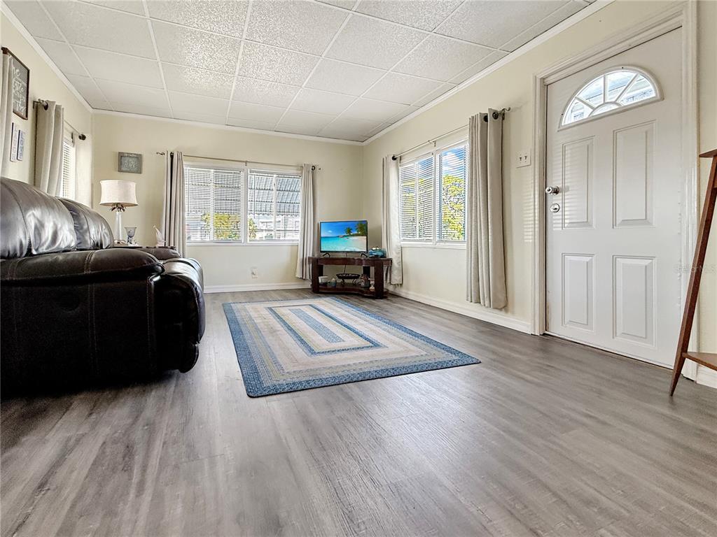 A living room features gray wood-look flooring, a drop ceiling, and a white front door — 5559 HOLIDAY PARK BOULEVARD, NORTH PORT, FL