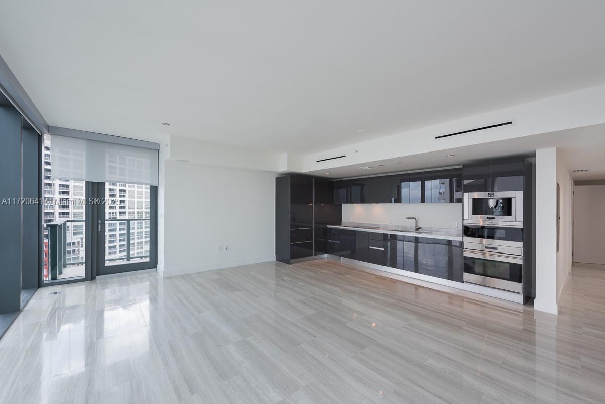 A modern kitchen with dark glossy cabinets and light tile flooring opens to a balcony — 1451 Brickell Ave # 2103, Miami FL 33131, MIAMI, FL