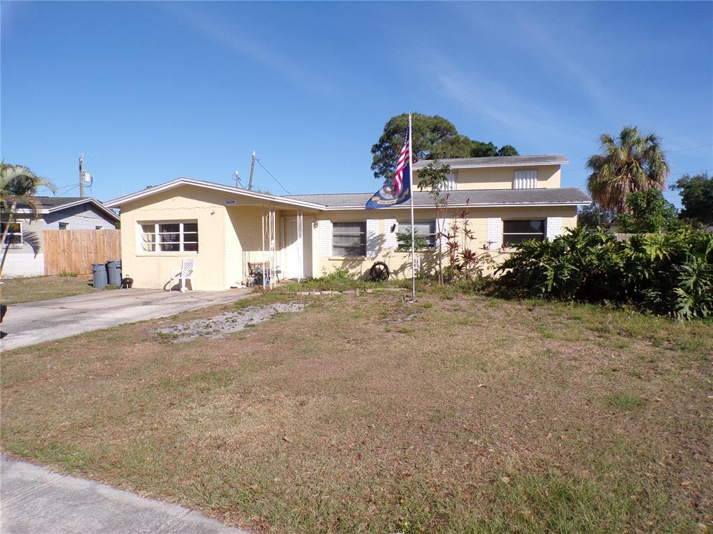 A single-story yellow house with a flag pole stands behind a dry grass lawn — 5606 87TH AVENUE N, PINELLAS PARK, FL