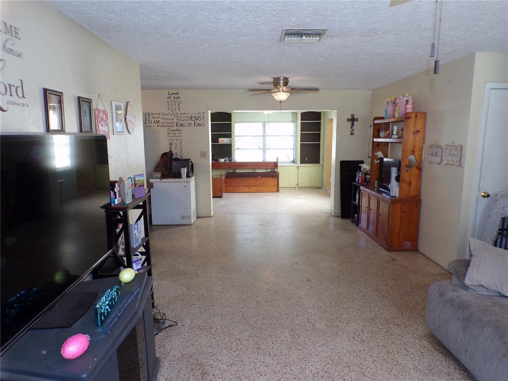 A living room with terrazzo flooring leads into a dining area with built-in shelving — 5606 87TH AVENUE N, PINELLAS PARK, FL