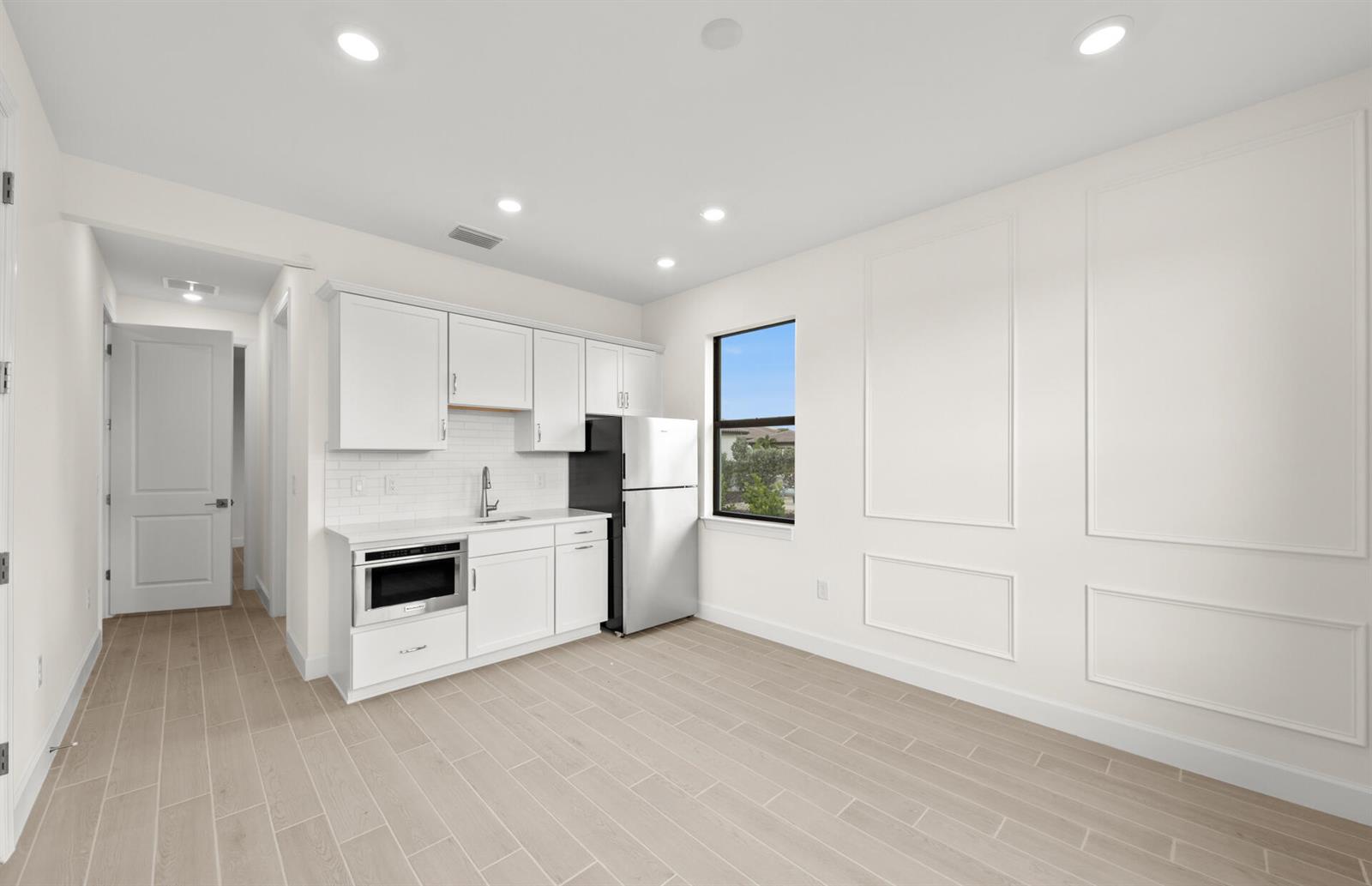 A kitchenette with white cabinets and a refrigerator sits in a room with paneled walls — 2034 Terreno Boulevard, Naples FL 34120, NAPLES, FL