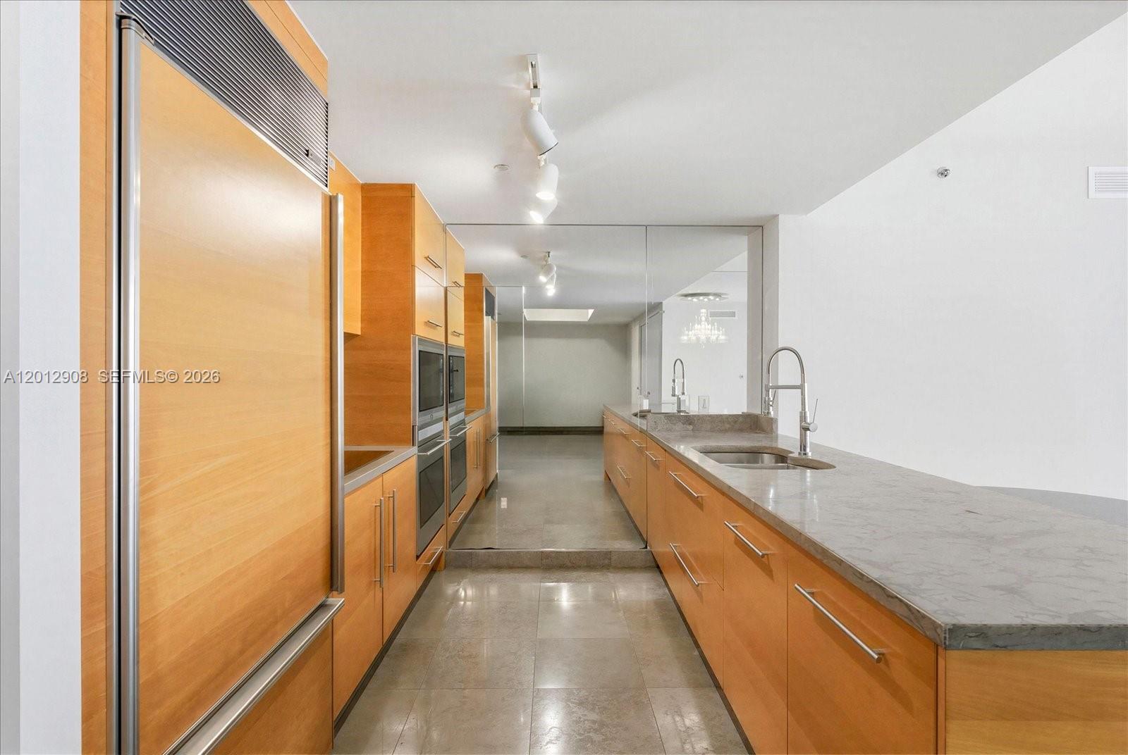 A galley kitchen features light wood cabinetry, stone countertops, and a full-height mirrored wall — 465 Brickell Ave # 4805, Miami FL 33131, MIAMI, FL