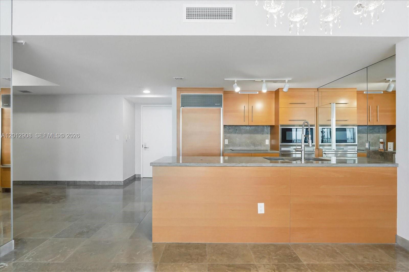 A modern kitchen features light wood cabinetry, a gray stone island, and polished tile floors — 465 Brickell Ave # 4805, Miami FL 33131, MIAMI, FL
