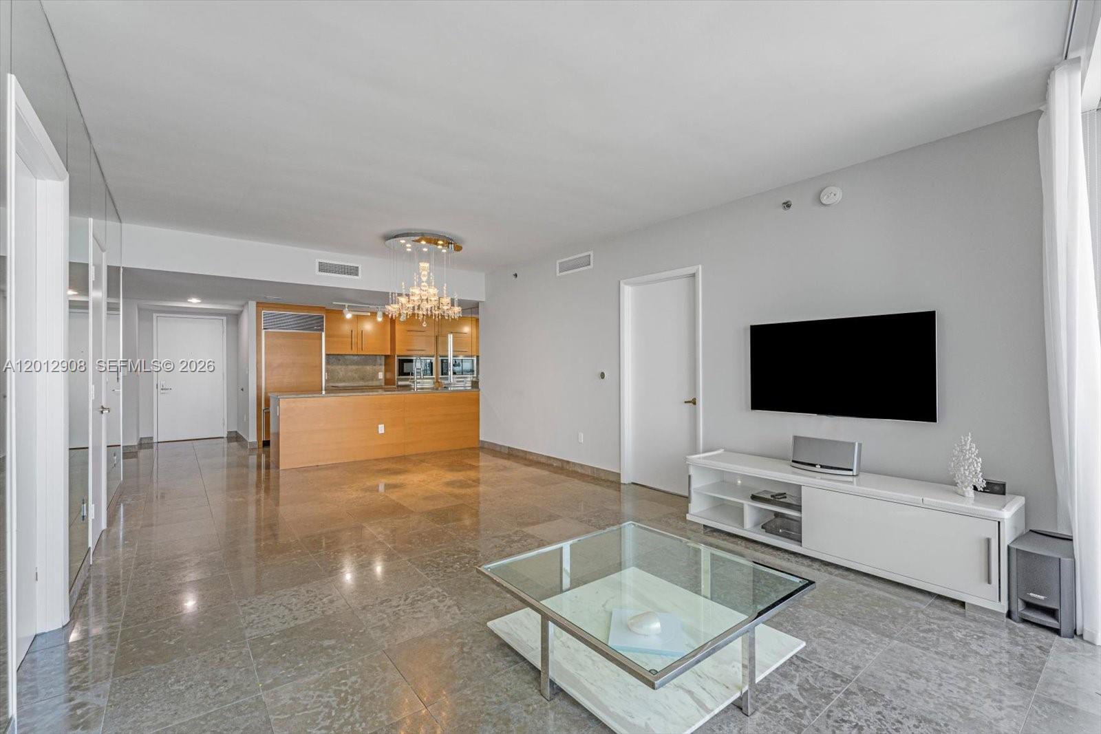 A modern living room features polished tile floors, a glass coffee table, and an open kitchen — 465 Brickell Ave # 4805, Miami FL 33131, MIAMI, FL