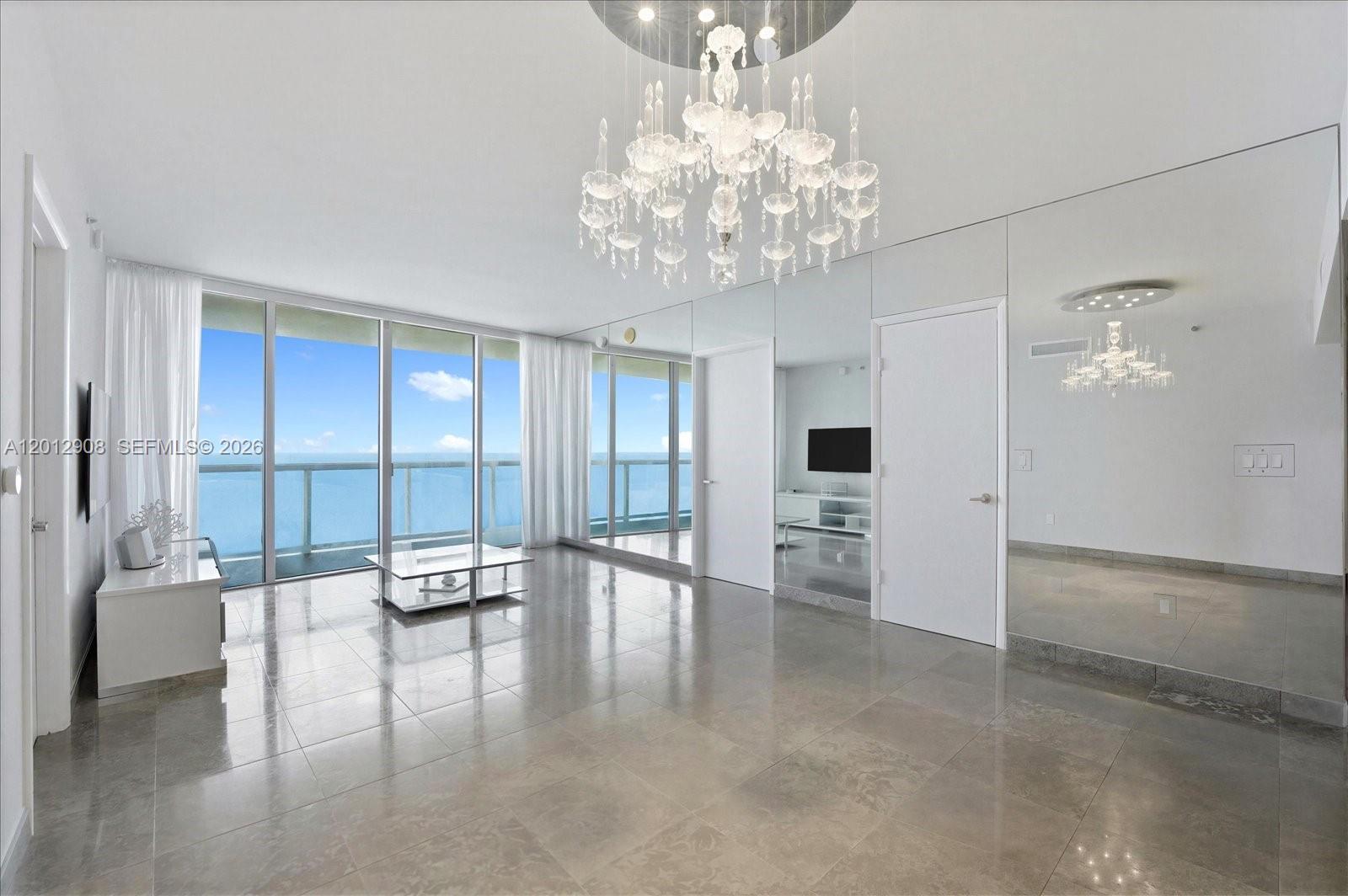 A living room features large floor-to-ceiling windows, tiled floors, a crystal chandelier, and mirrored walls — 465 Brickell Ave # 4805, Miami FL 33131, MIAMI, FL