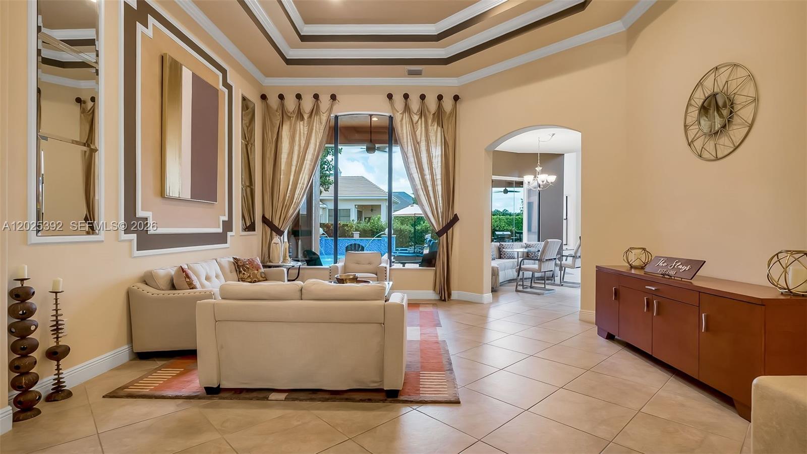 A living room features a tray ceiling, beige walls, tile floors, and a pool view — 8891 Equus Cir, Boynton Beach FL 33472, BOYNTON BEACH, FL