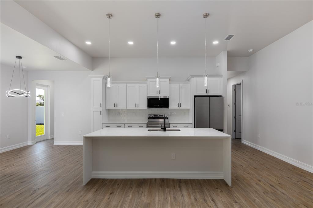 A modern kitchen features white cabinetry, a central island, stainless steel appliances, and wood flooring — 521 NW 5TH STREET, CAPE CORAL, FL