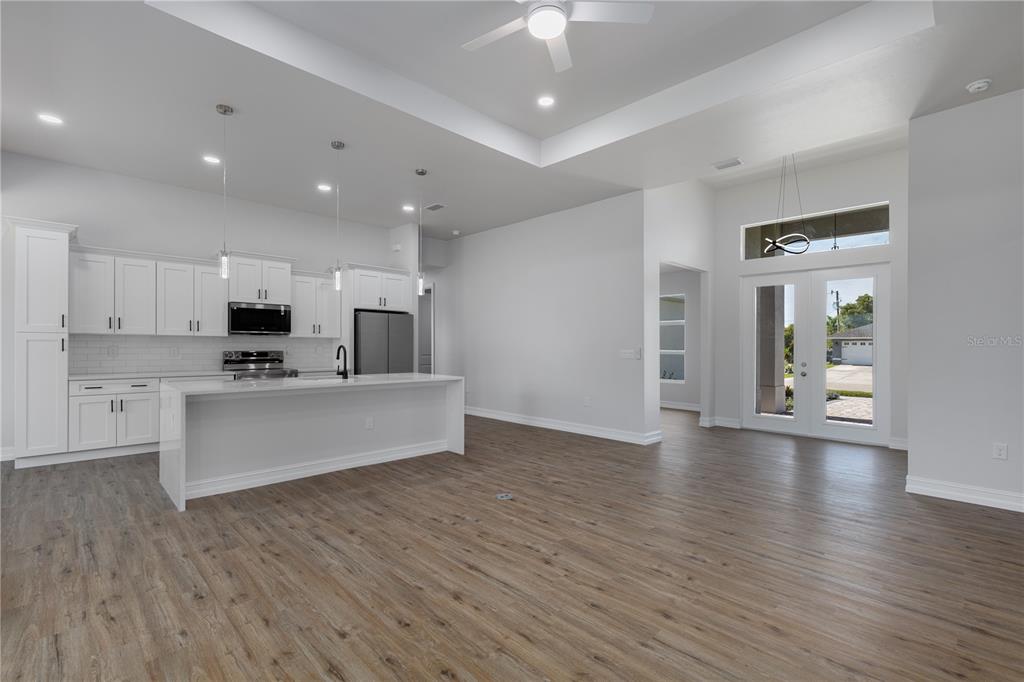 A modern open-concept kitchen and living area with white cabinetry, a large island, and wood-look flooring — 521 NW 5TH STREET, CAPE CORAL, FL