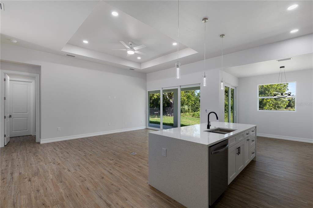 A modern open-concept kitchen and living area features a white island, pendant lighting, and wood-look flooring — 521 NW 5TH STREET, CAPE CORAL, FL