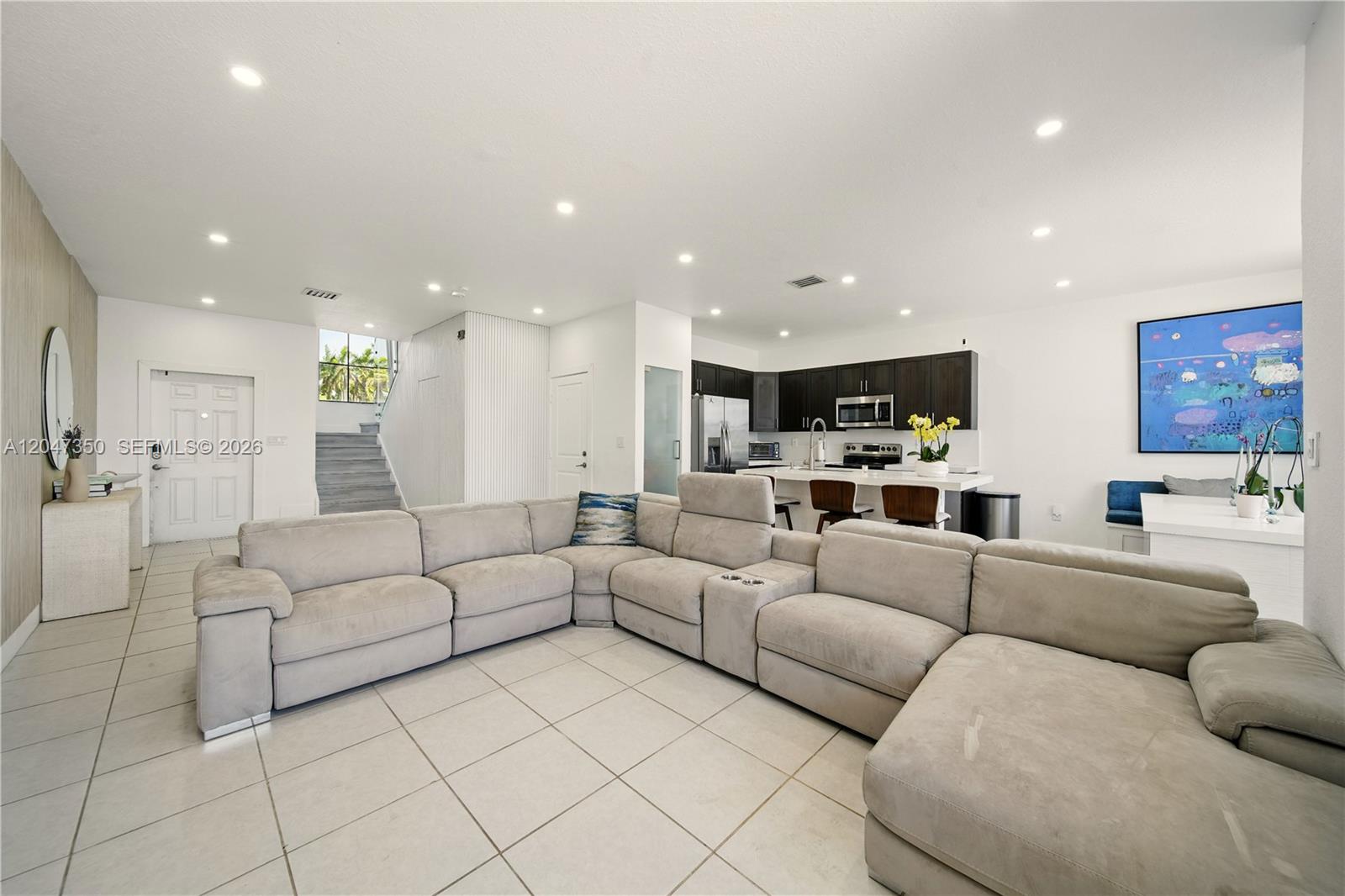 A large, open-concept living room features a light gray sectional sofa and a modern kitchen — 10269 SW 231st Ln # 0, Miami FL 33190, MIAMI, FL