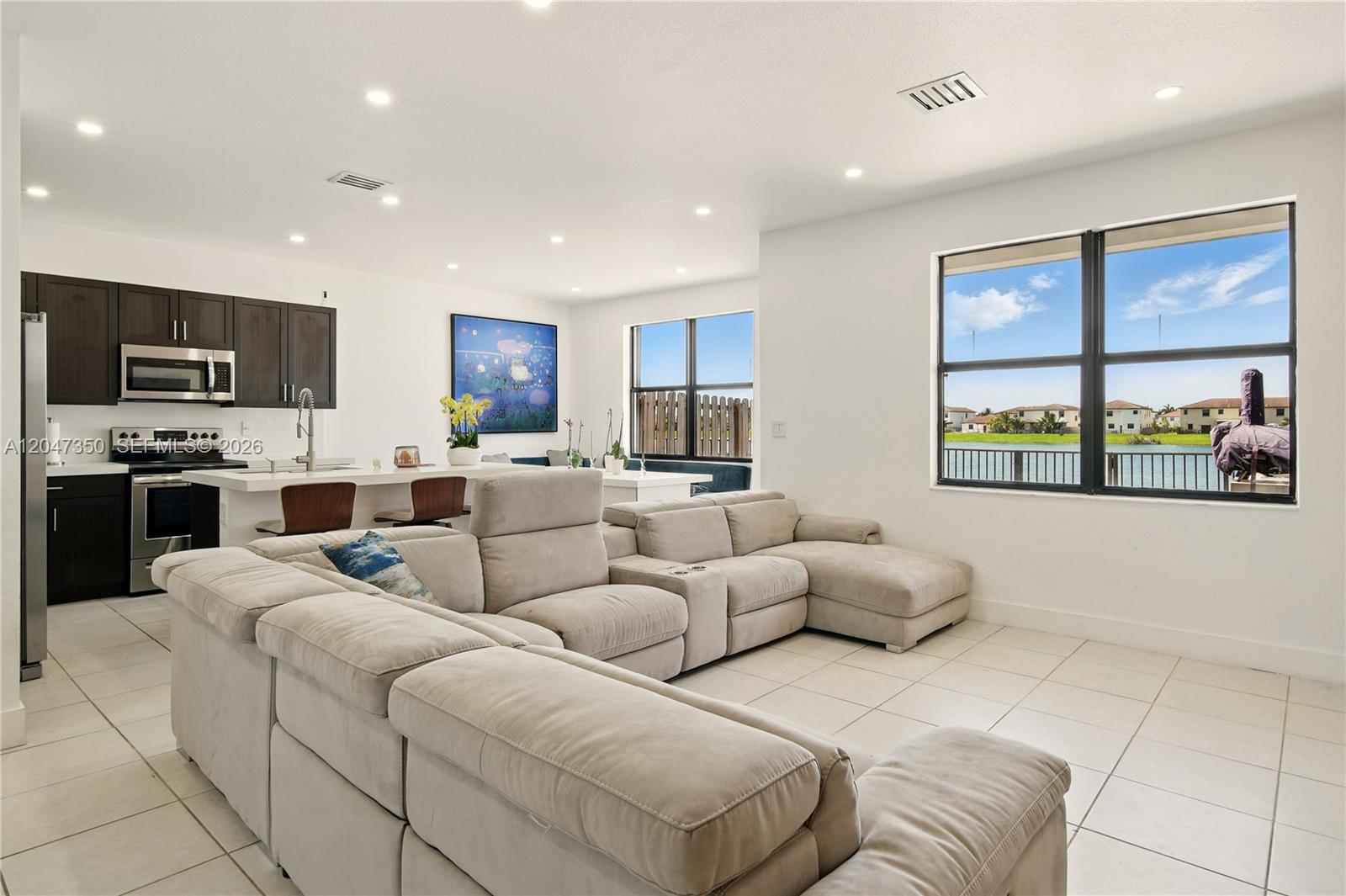 A modern open-concept living room features a large sectional sofa, kitchen, and lake views — 10269 SW 231st Ln # 0, Miami FL 33190, MIAMI, FL