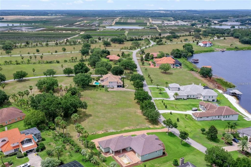 An aerial view shows several large houses with swimming pools situated on a grassy lakefront lot — 17152 ROYAL PALM DRIVE, GROVELAND, FL