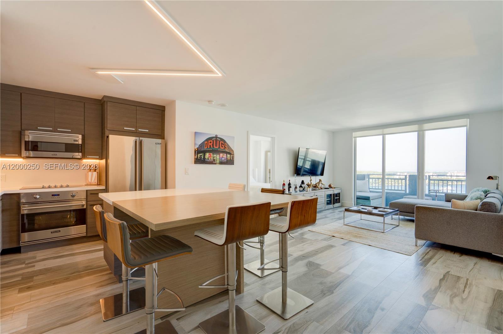 A modern open-concept kitchen and living area features wood cabinetry, a breakfast island, and balcony — 90 Alton Rd # 2010, Miami Beach FL 33139, MIAMI BEACH, FL