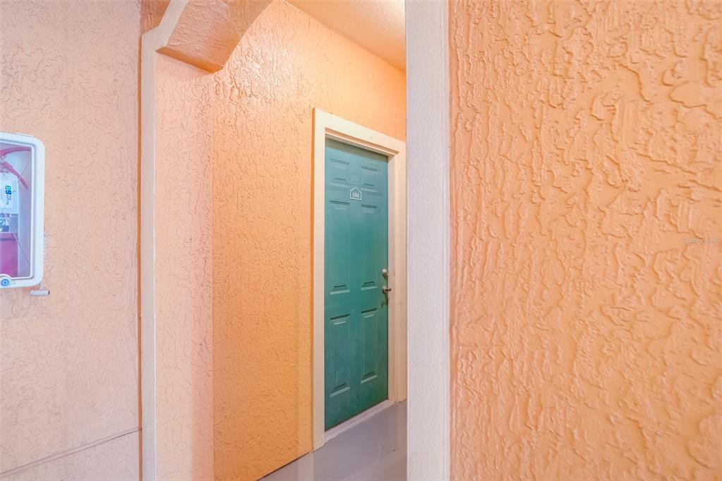 A teal door is recessed within a peach-colored stucco hallway — 2741 VIA CIPRIANI UNIT 930A, CLEARWATER, FL