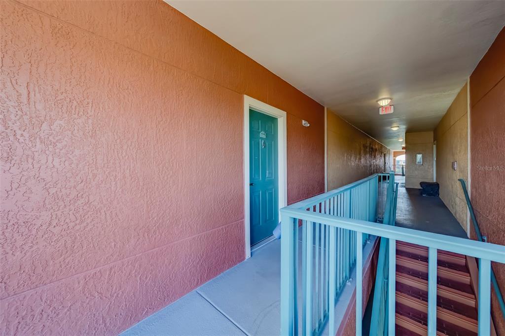 An exterior walkway with a teal door, blue railing, and stairs leading to a hallway — 2741 VIA CIPRIANI UNIT 930A, CLEARWATER, FL