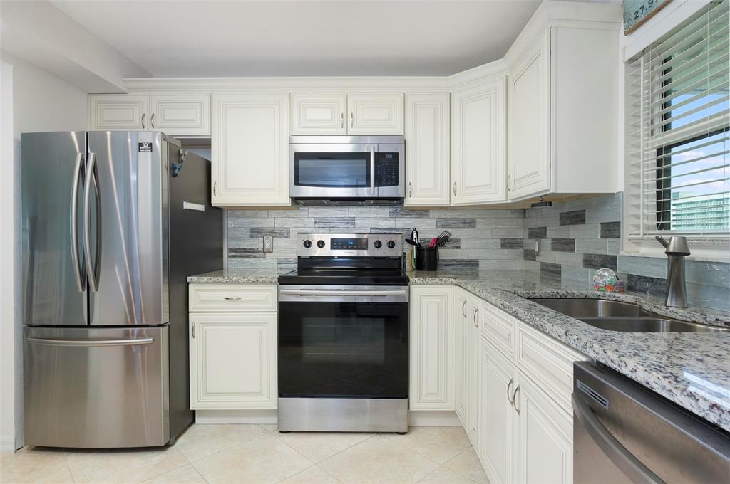 A kitchen with white cabinets, stainless steel appliances, granite countertops, and a tiled backsplash — 1230 GULF BOULEVARD UNIT 608, CLEARWATER BEACH, FL